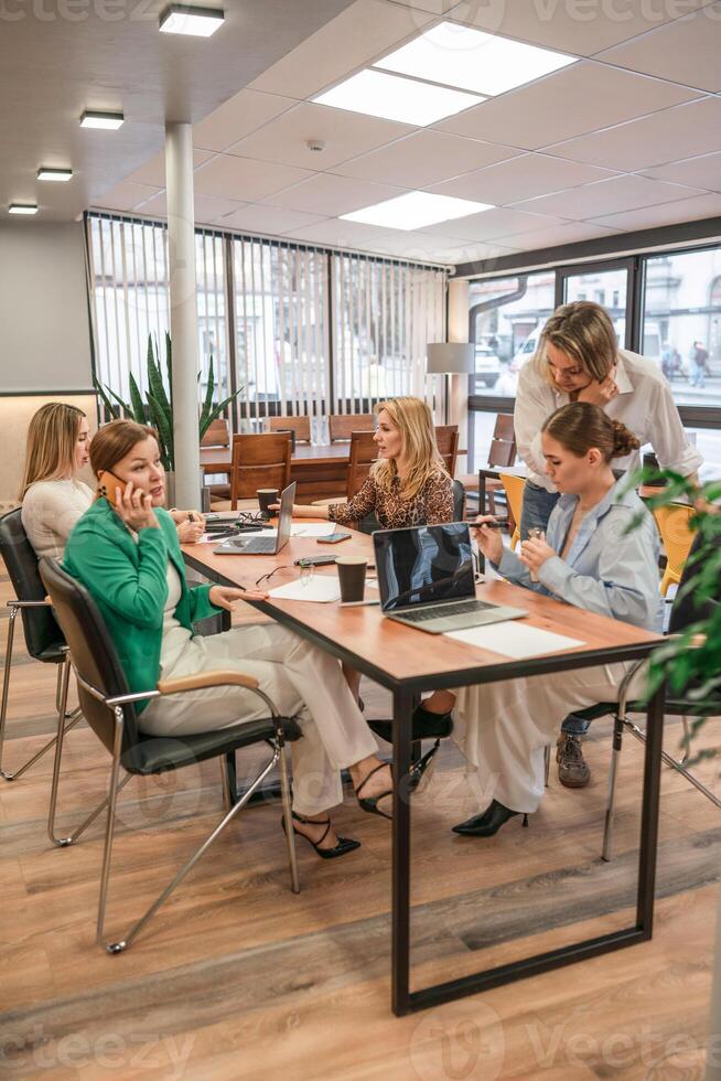 Businesswomen Meeting Laptops. Team collaborates at office table for strategy session, daytime work talk. photo