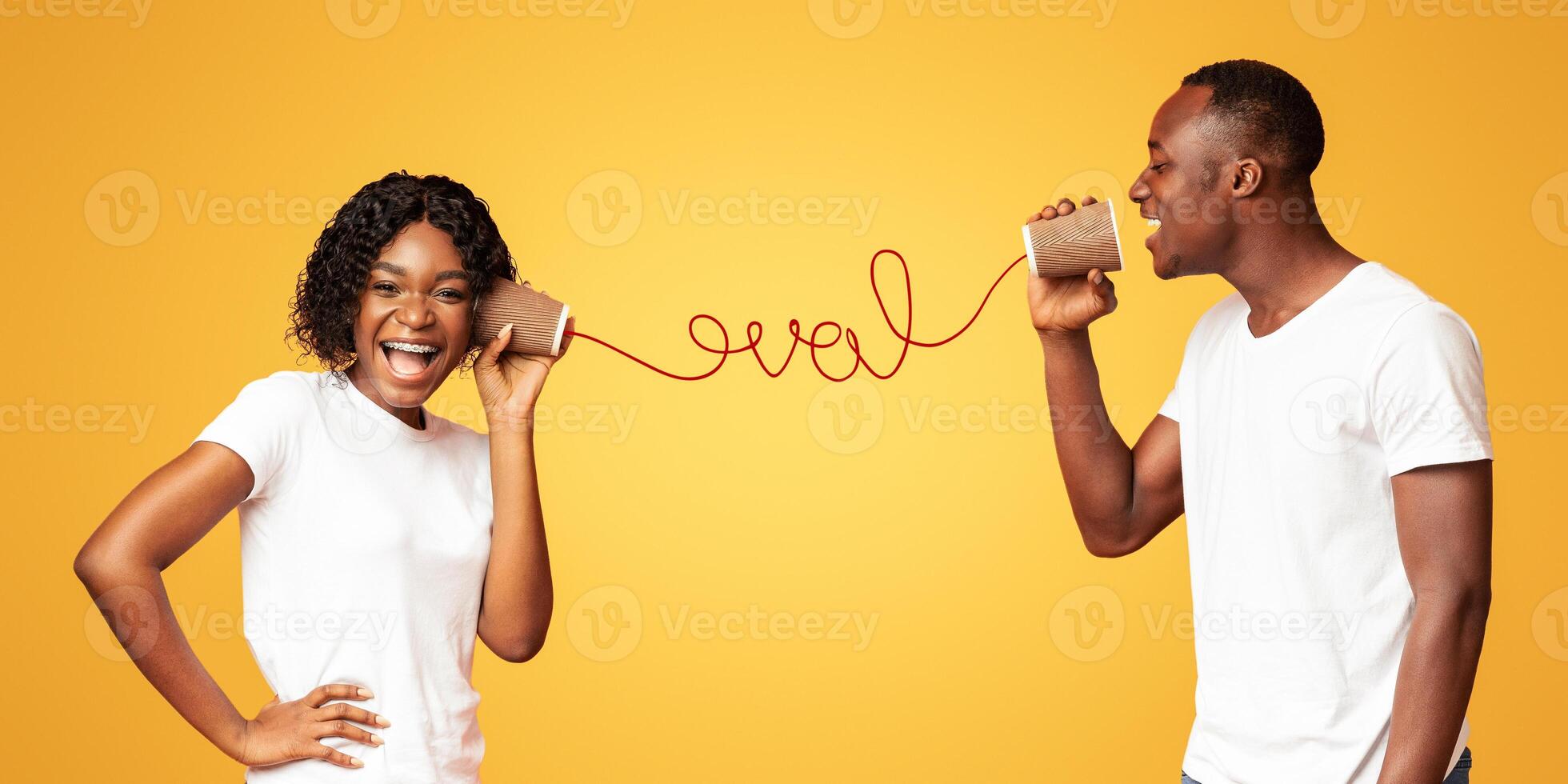 African american guy saying words of love to his happy girlfriend, standing on orange background and using tin can phone, having red love word between them. Love, relationships concept photo