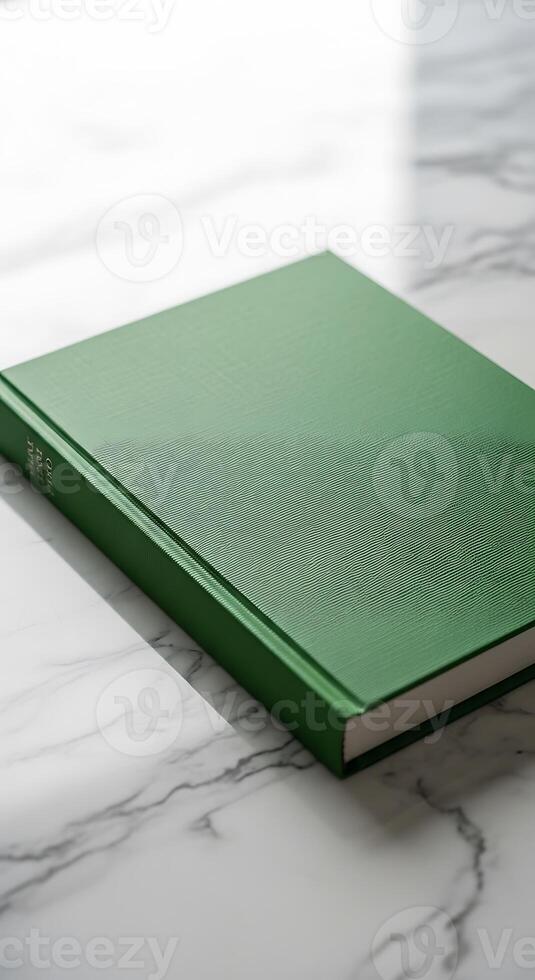 A close up shot of a green book lying flat on a white marble surface in soft natural lighting photo