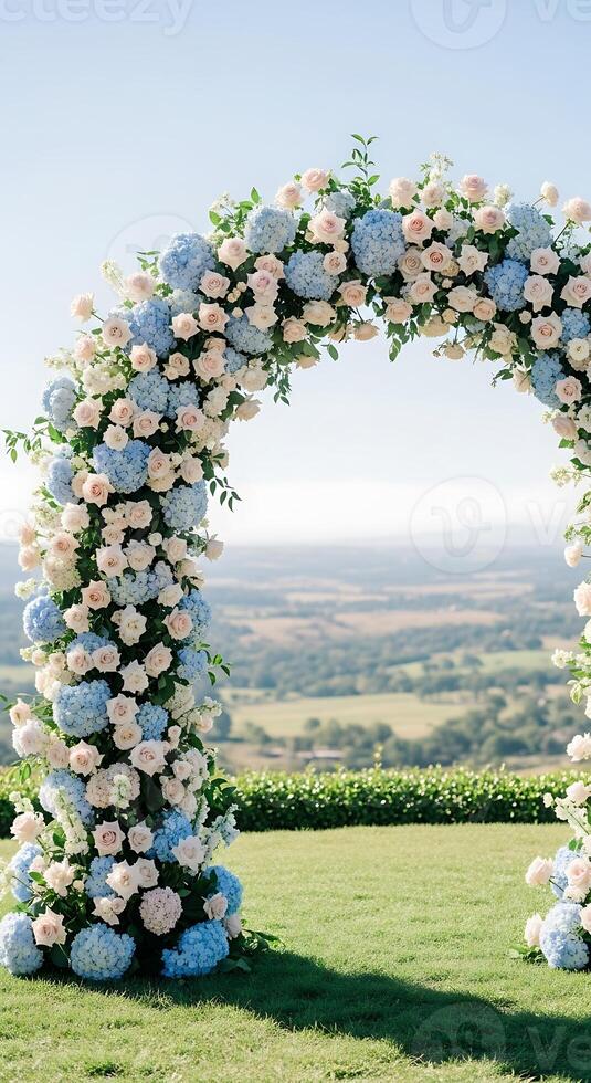 Floral archway with blue hydrangeas and pink roses overlooking a green landscape on a sunny day photo