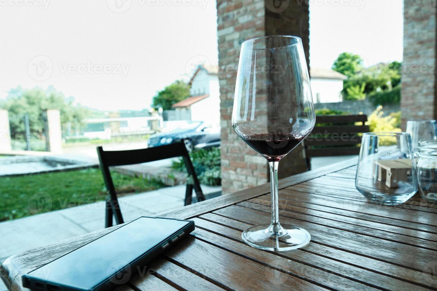 Glass of wine with a cell phone next to it on a table in the greenery of an Italian garden photo