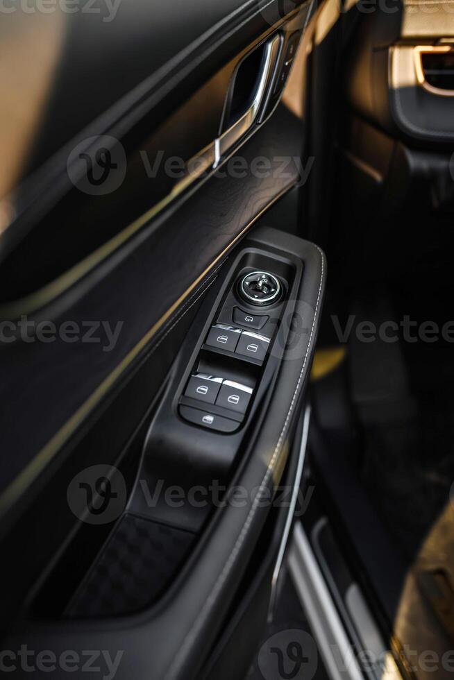 Close-up of car door panel featuring control buttons for windows and mirrors, black leather trim with white stitching, chrome handle and ambient lighting. Modern, elegant design. photo