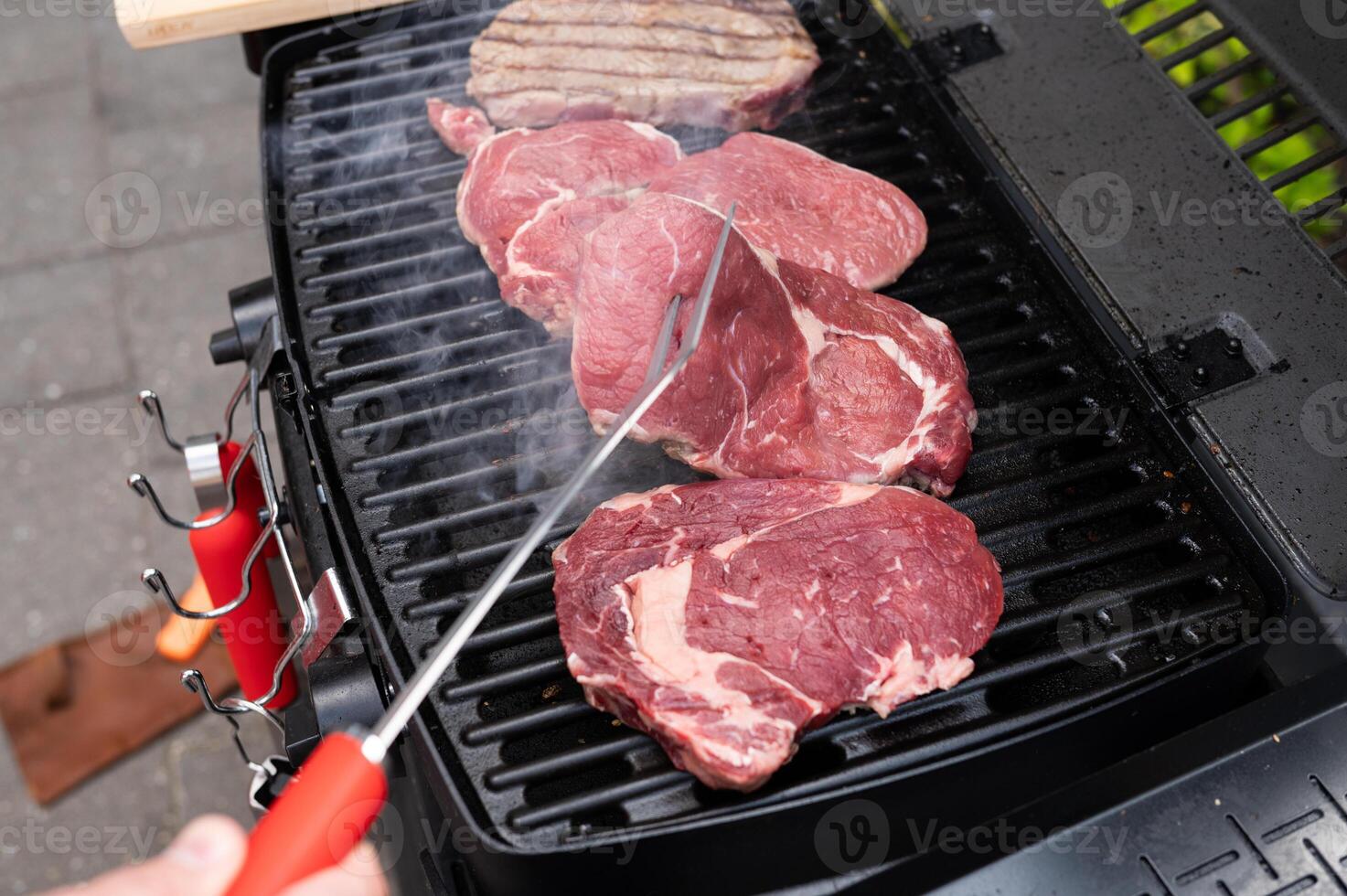 Grilling juicy steaks on outdoor barbecue grill with smoke rising in backyard photo