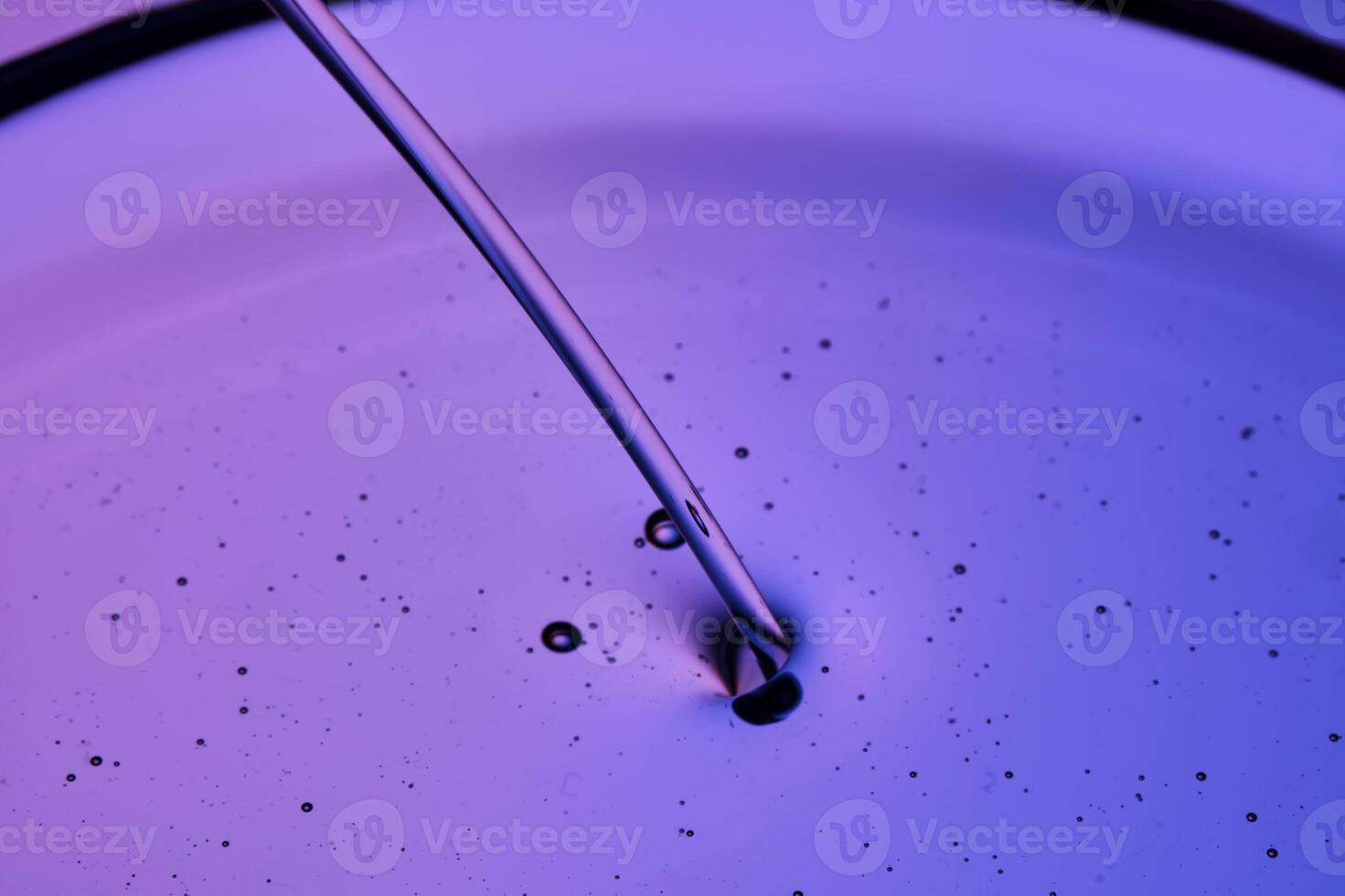 A jet of facial oil flowing into a petri dish on a purple background. photo