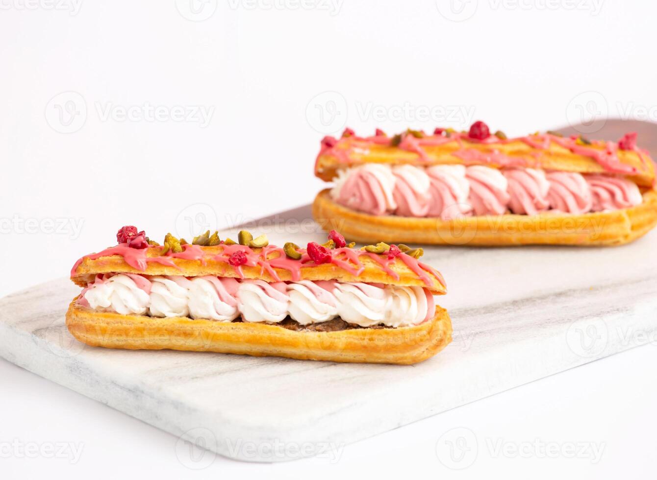 Gourmet Pink Eclairs with Cream Filling, Pistachios and Dried Raspberries on marble board side view of dessert menus photo