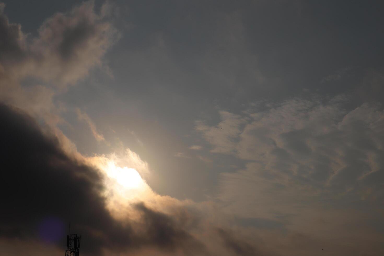 Sun shining through scattered clouds in a sky transitioning from orange to gray photo