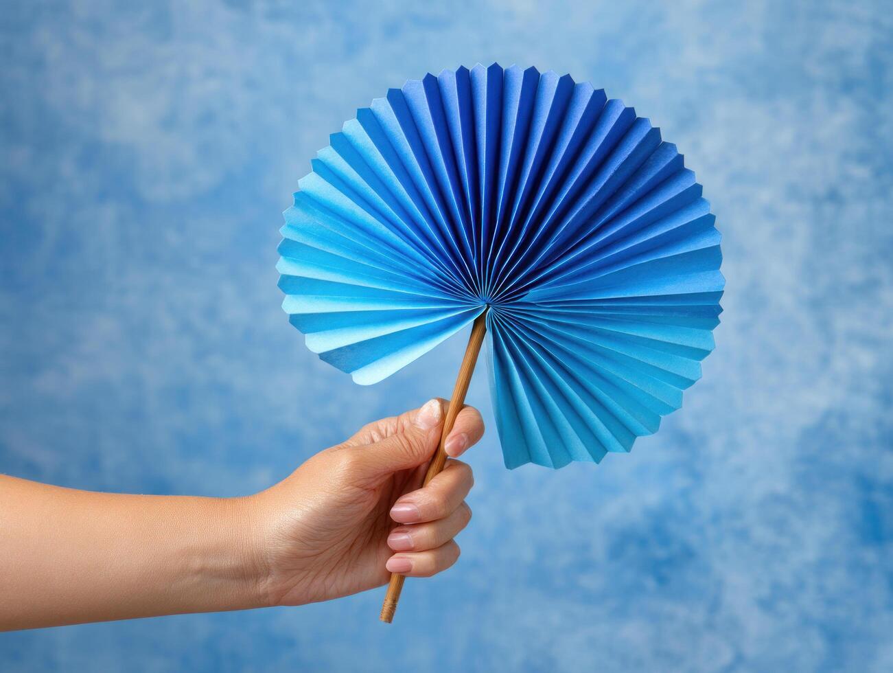 Blue paper fan held by hand with wooden handle against blue textured background, creating calm and refreshing atmosphere photo