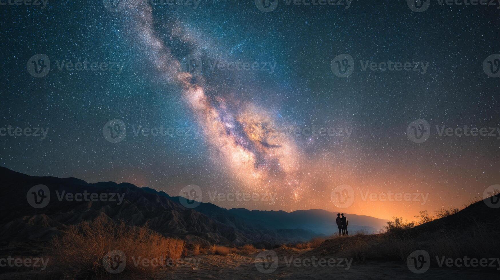 Romantic couple gazing at the starry night sky with a vibrant Milky Way galaxy over mountains in a serene landscape photo