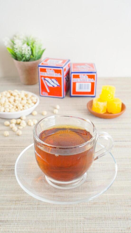 Yogyakarta, Indonesia, 2025 - A cup of Bendera tea brand accompanied by sugar cubes and snacks on wooden table isolated on light background photo