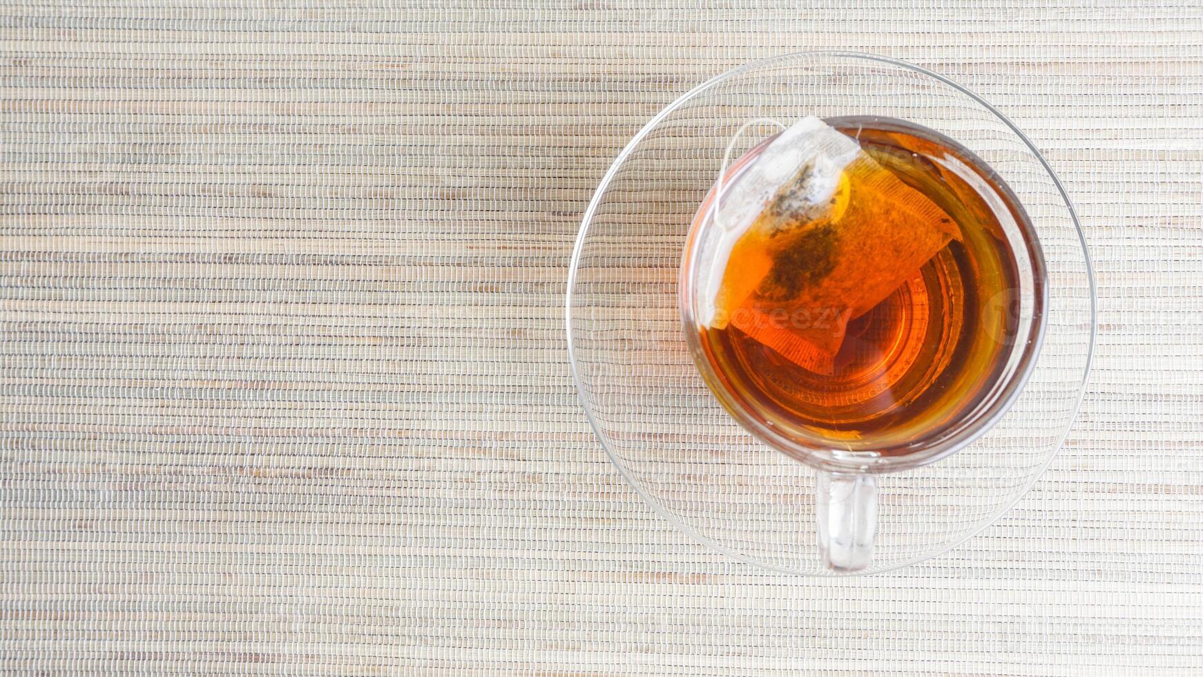 Top view of a transparent glass cup of tea with teabag isolated on wooden texture background photo