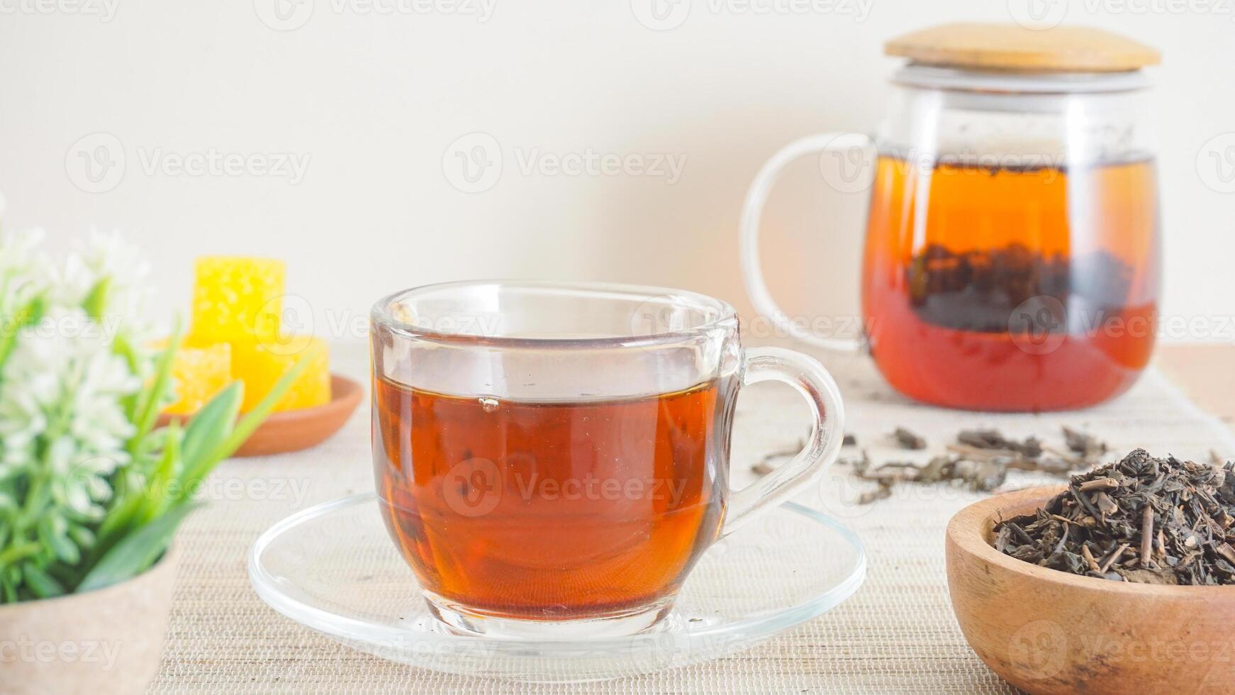 A clear cup of tea, a clear teapot, and sugar cubes on wooden table isolated on light background photo