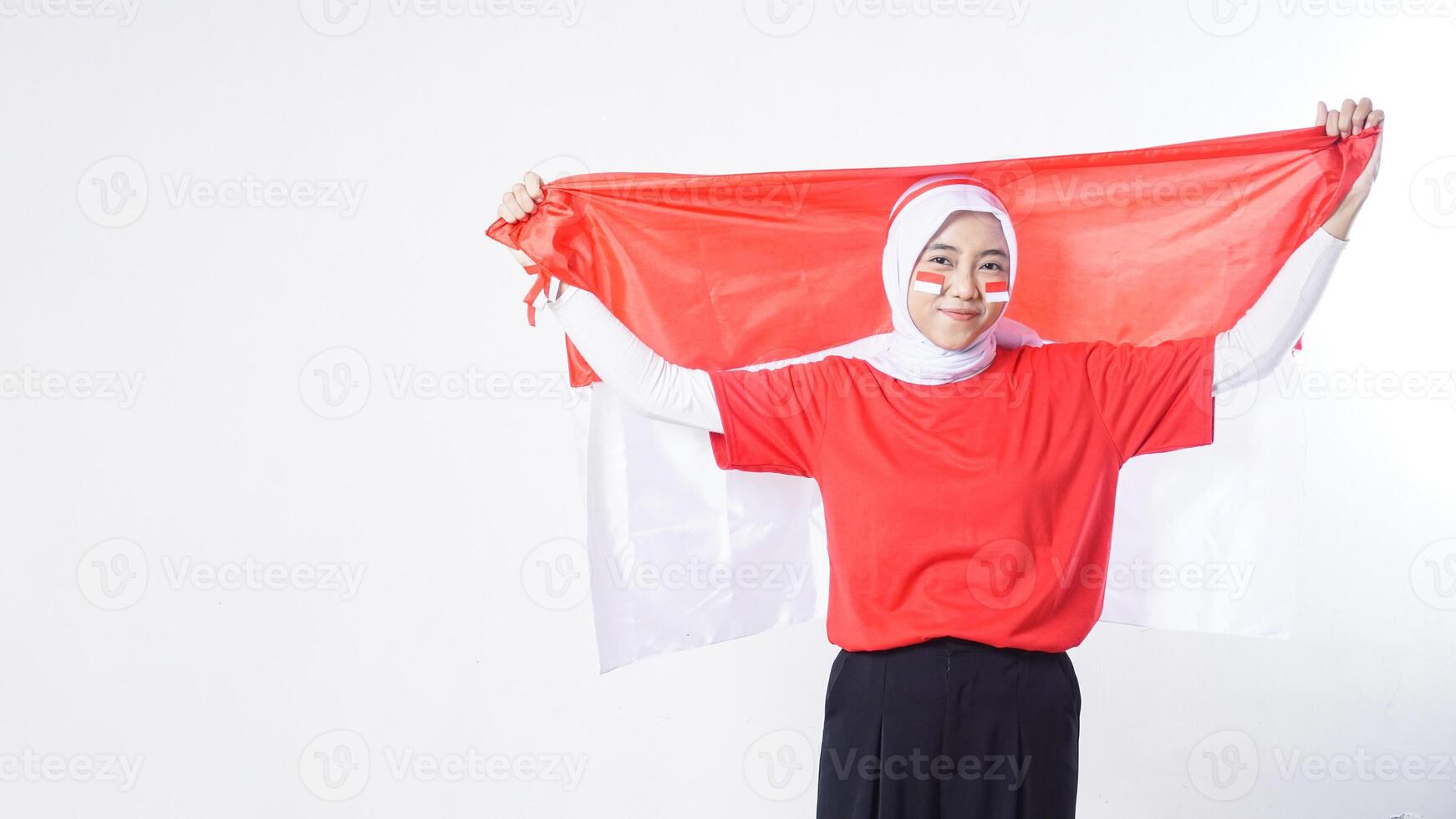 Beautiful muslim Asian girl celebrate Indonesia independence day in red and white outfit holding Indonesian flag above her head isolated on white background photo