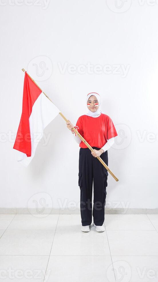 Beautiful muslim Asian girl celebrate Indonesia independence day in red and white outfit by holding Indonesian flag isolated on white background photo