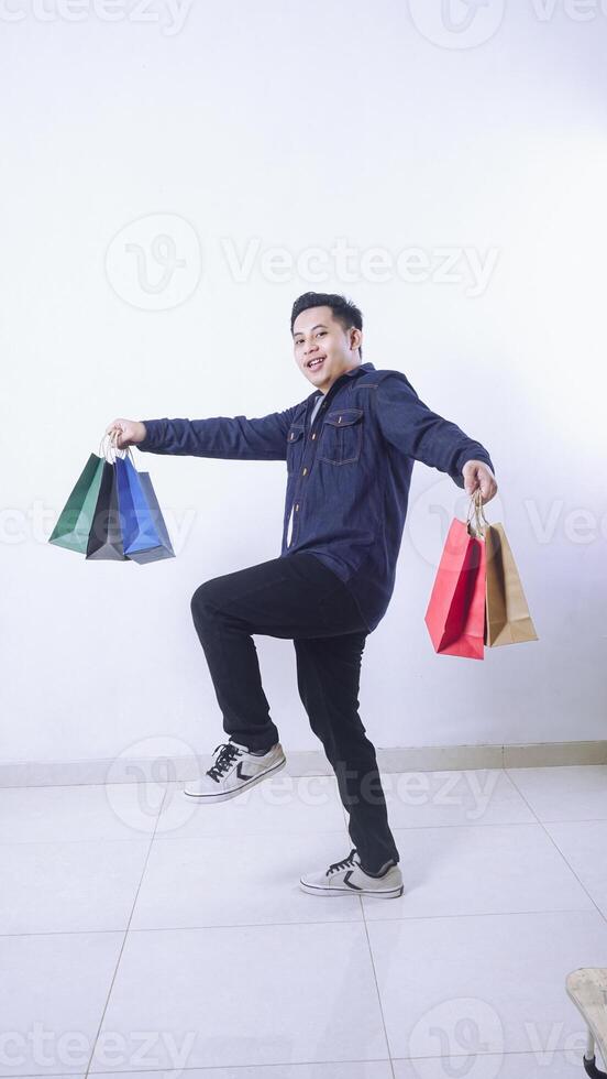 Full length photo of Asian man carrying many shopping bags with excitement isolated on white background