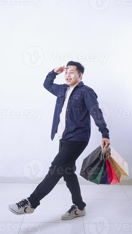 Full length photo of Asian man walking while holding shopping bags with excitement isolated on white background