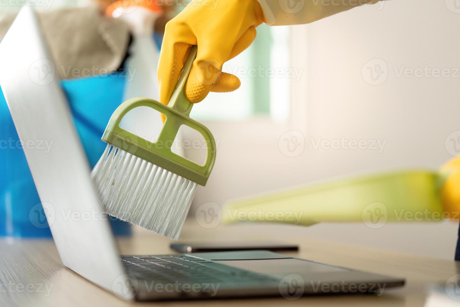 Home Cleaning. Woman using brush to clean laptop with yellow rubber gloves. photo