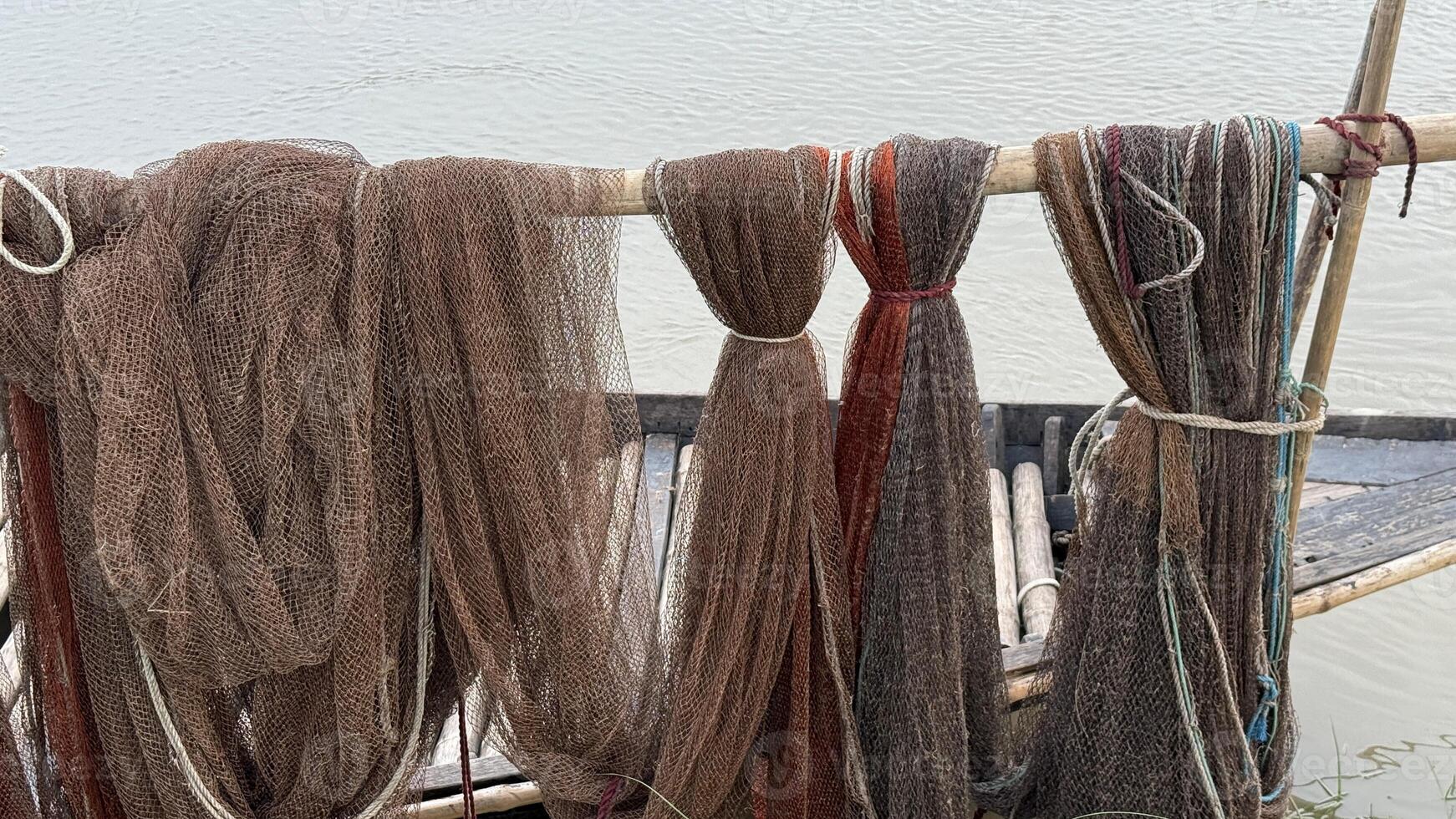 Several old brown fishing nets hang knotted on a wooden structure over the water photo