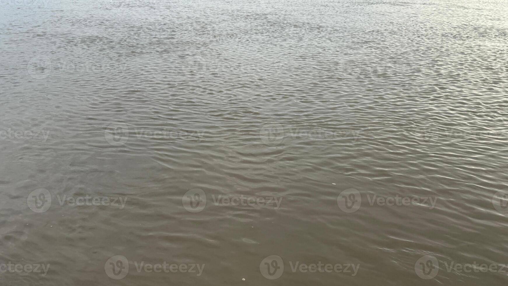 The flowing river reflects sky and light, creating an abstract water surface texture photo