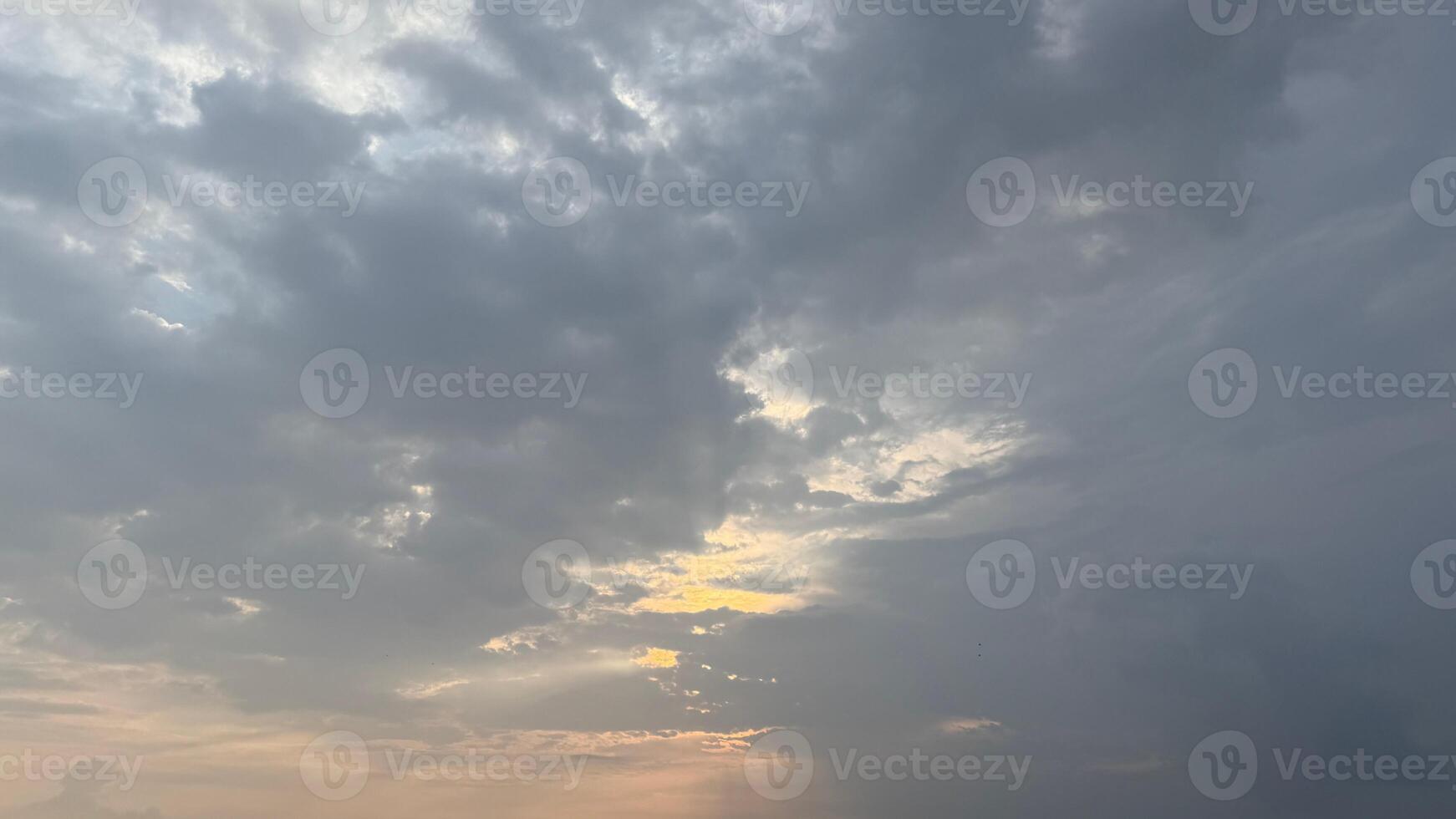 Moody gray cloudscape reveals the sun peeking through, creating soft light rays across the sky photo