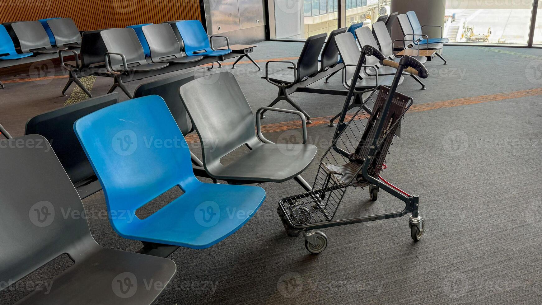 An abandoned luggage trolley rests among stark airport seating, evoking the transient echoes of missed connections and Laylat al Miraj dreams photo