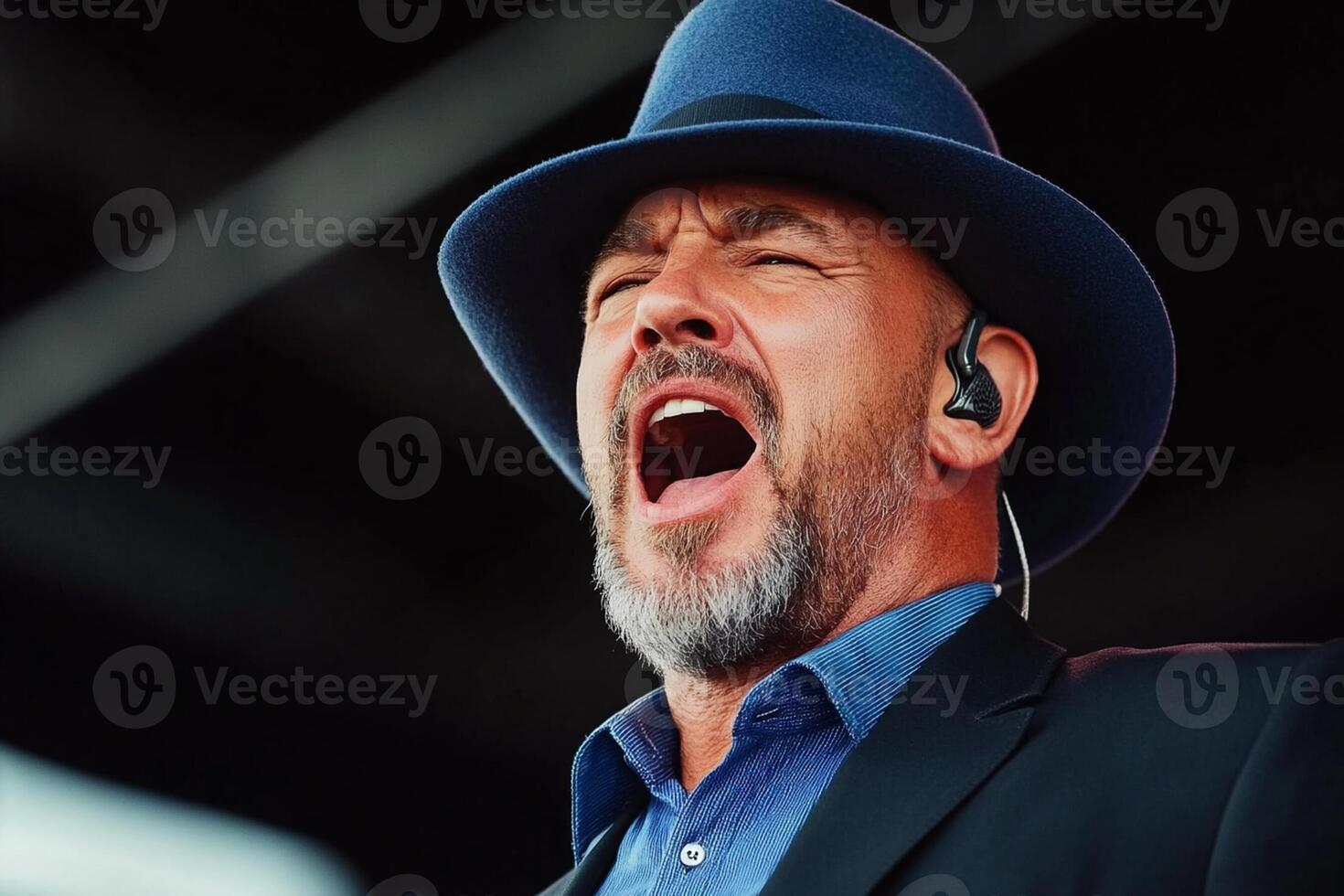 A man in a blue hat singing into a microphone photo