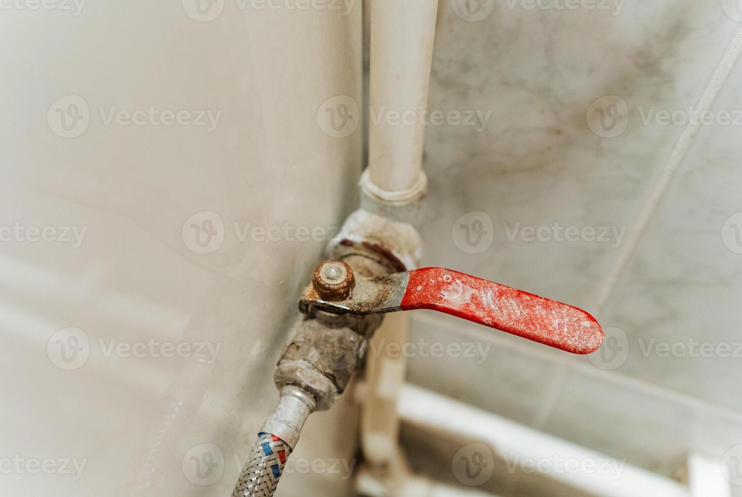 This image showcases a detailed closeup of a vibrant red valve located on a water pipe, illustrating the crucial components of a plumbing system in a household environment photo