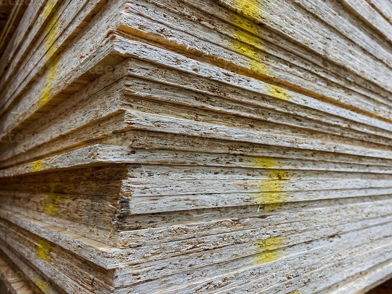 This image shows a detailed close up of a neatly arranged stack of plywood sheets, each featuring distinct yellow markings on their surface, indicating measurements or grades photo