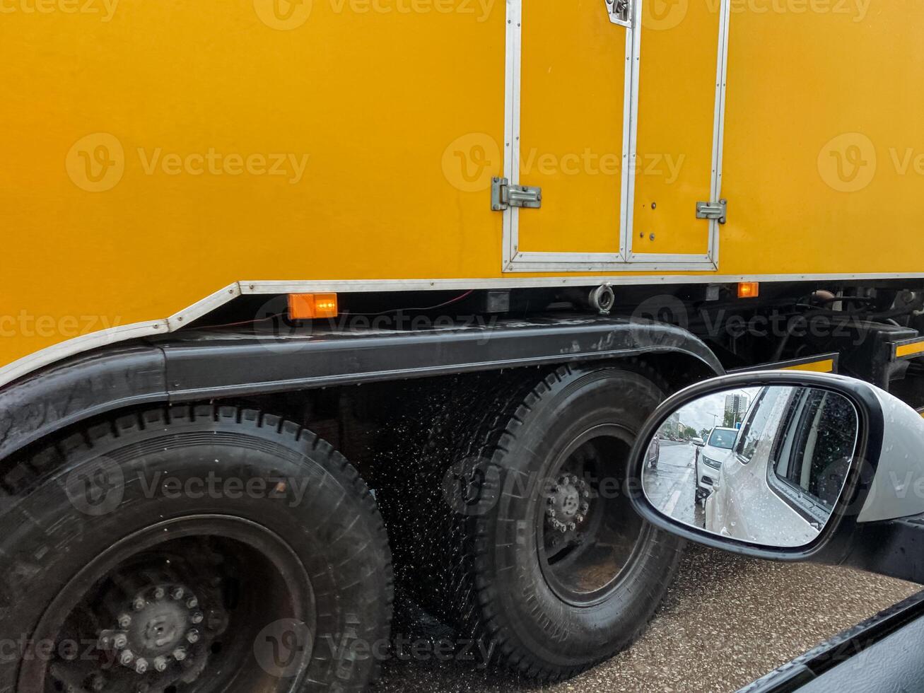 A closeup of a bright yellow truck showcases its robust tires and shiny side mirror, highlighting the vehicles industrial strength and versatile capabilities in various applications photo