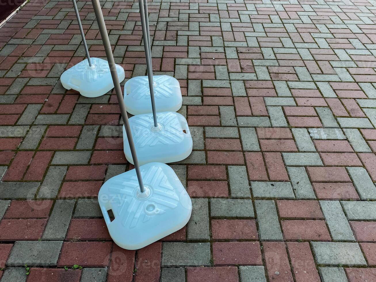 A neat row of white plastic containers is arranged meticulously on a sturdy brick pavement, showcasing a striking design that stands out against the textured surface beneath them photo
