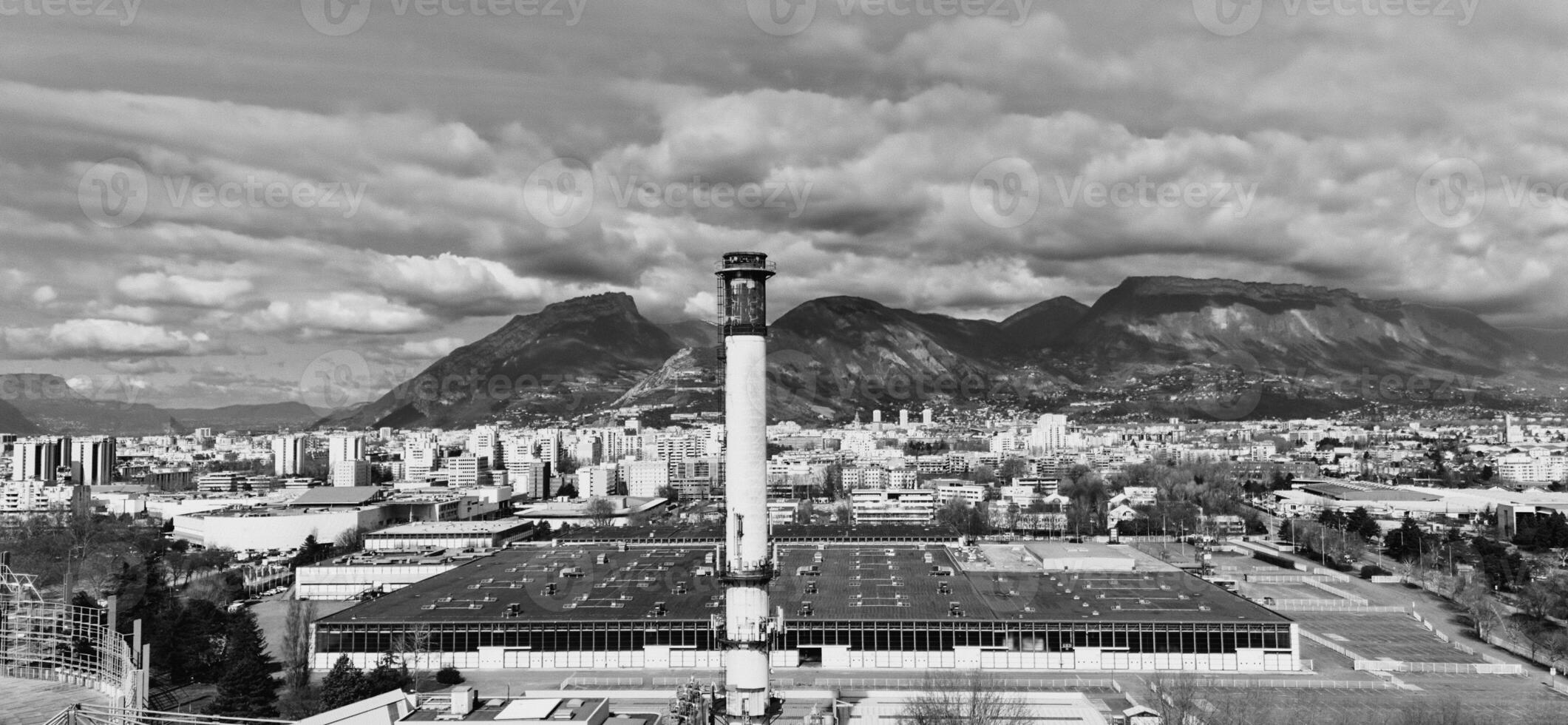 Black and white photo of industrial chimney and city skyline with mountains