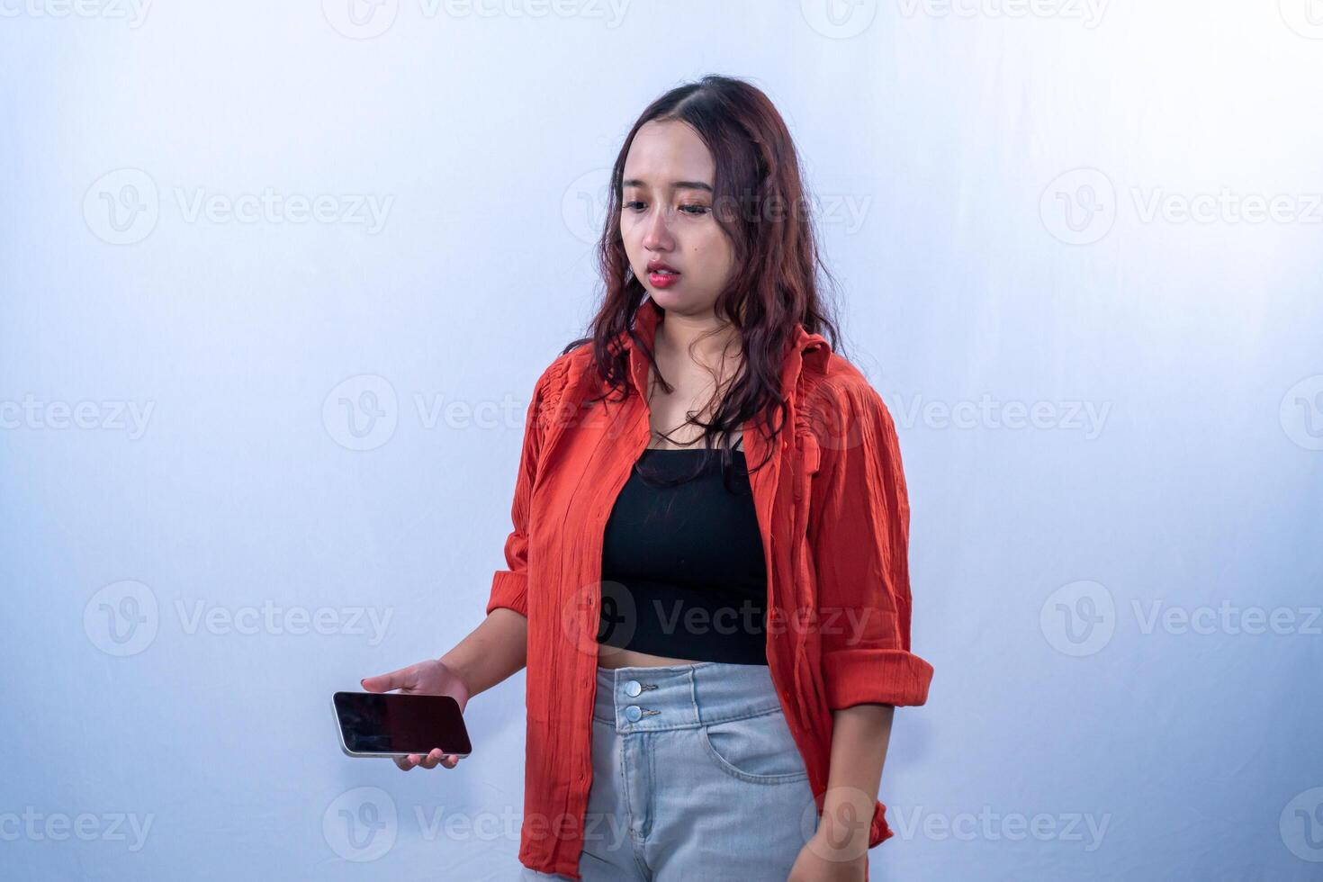 Indonesian Asian woman wearing orange shirt holding cellphone and looking down at her lips photo