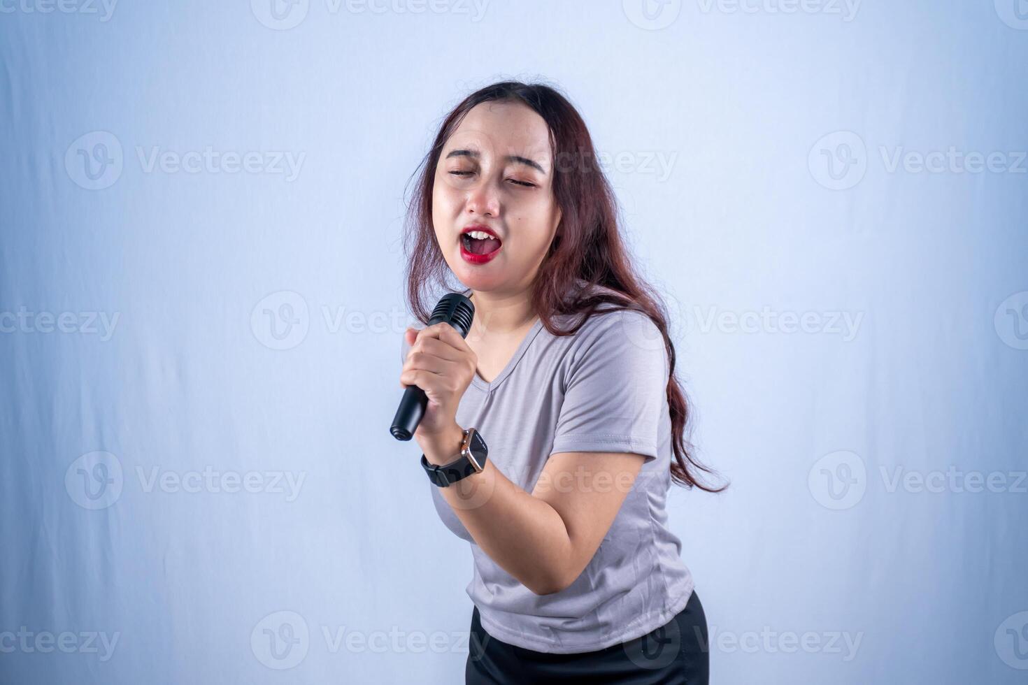 A young Asian woman intensely sings into a microphone, her eyes closed and mouth open wide, fully immersed in her vocal performance. photo