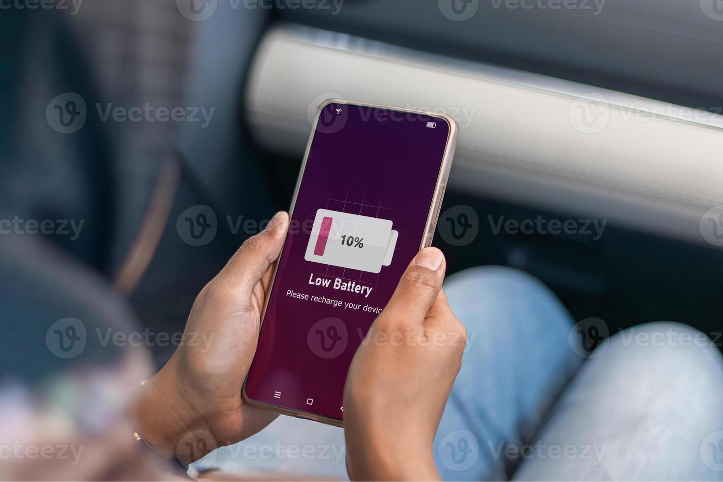 Running out of battery while on the go. A muslim woman in car holding a smartphone with low battery symbol on screen. photo