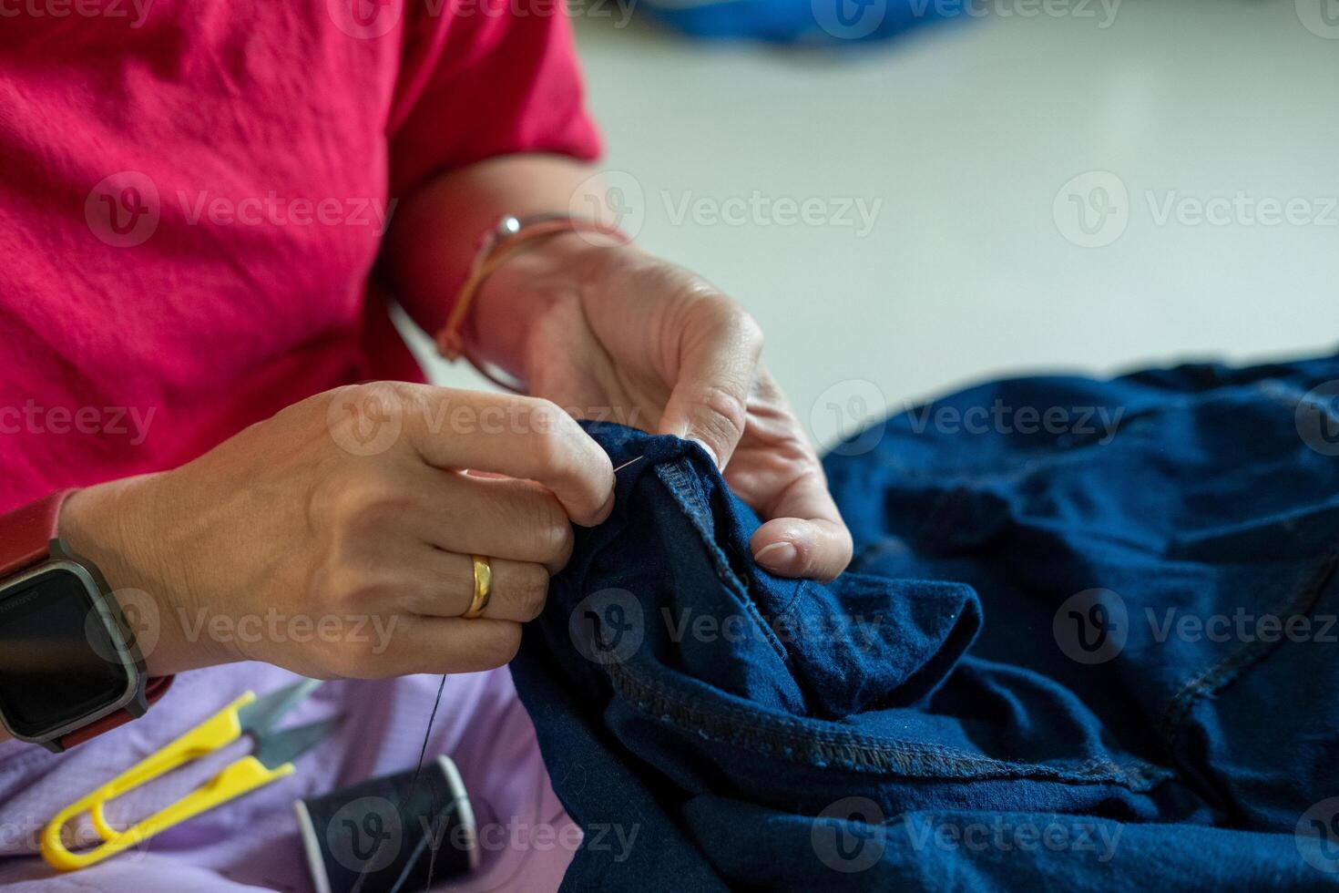 Caring mother repairing her child trousers by hand, focusing on sewing trouser legs. photo