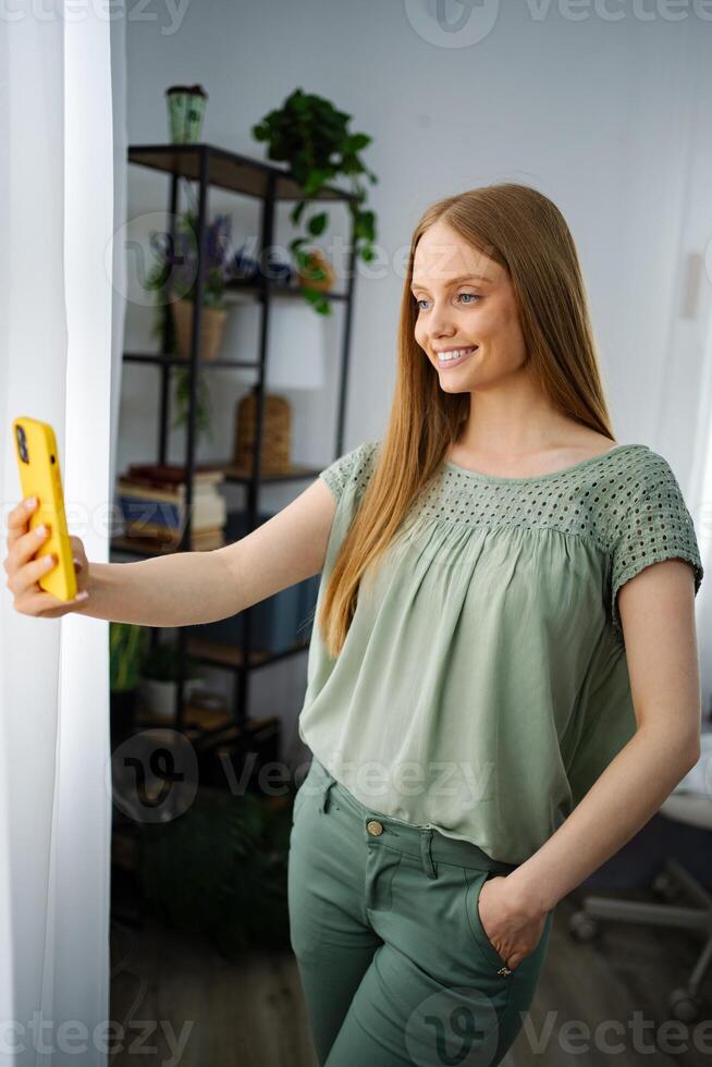 Smiling woman takes a selfie in a cozy indoor setting with plants photo