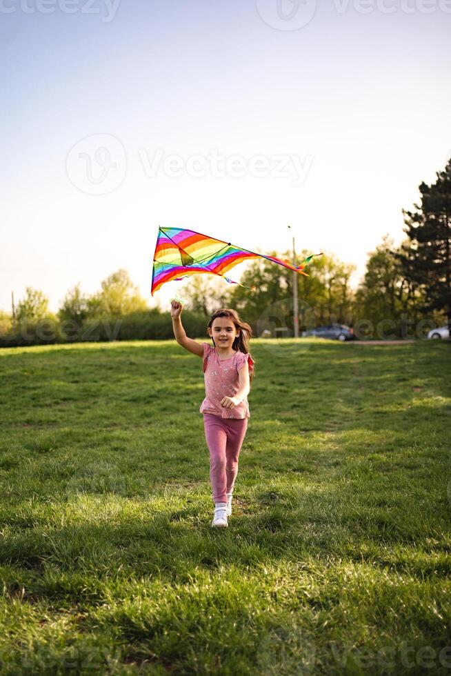Joyful girl runs with colorful kite in sunny park photo