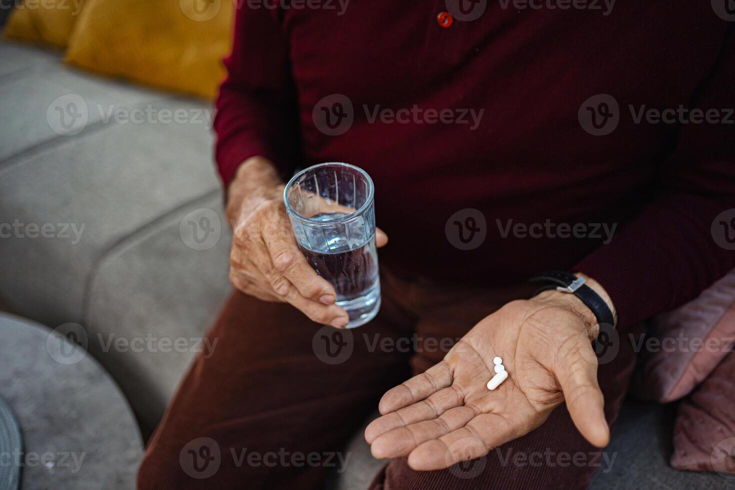 Older man taking medication with glass of water at home photo