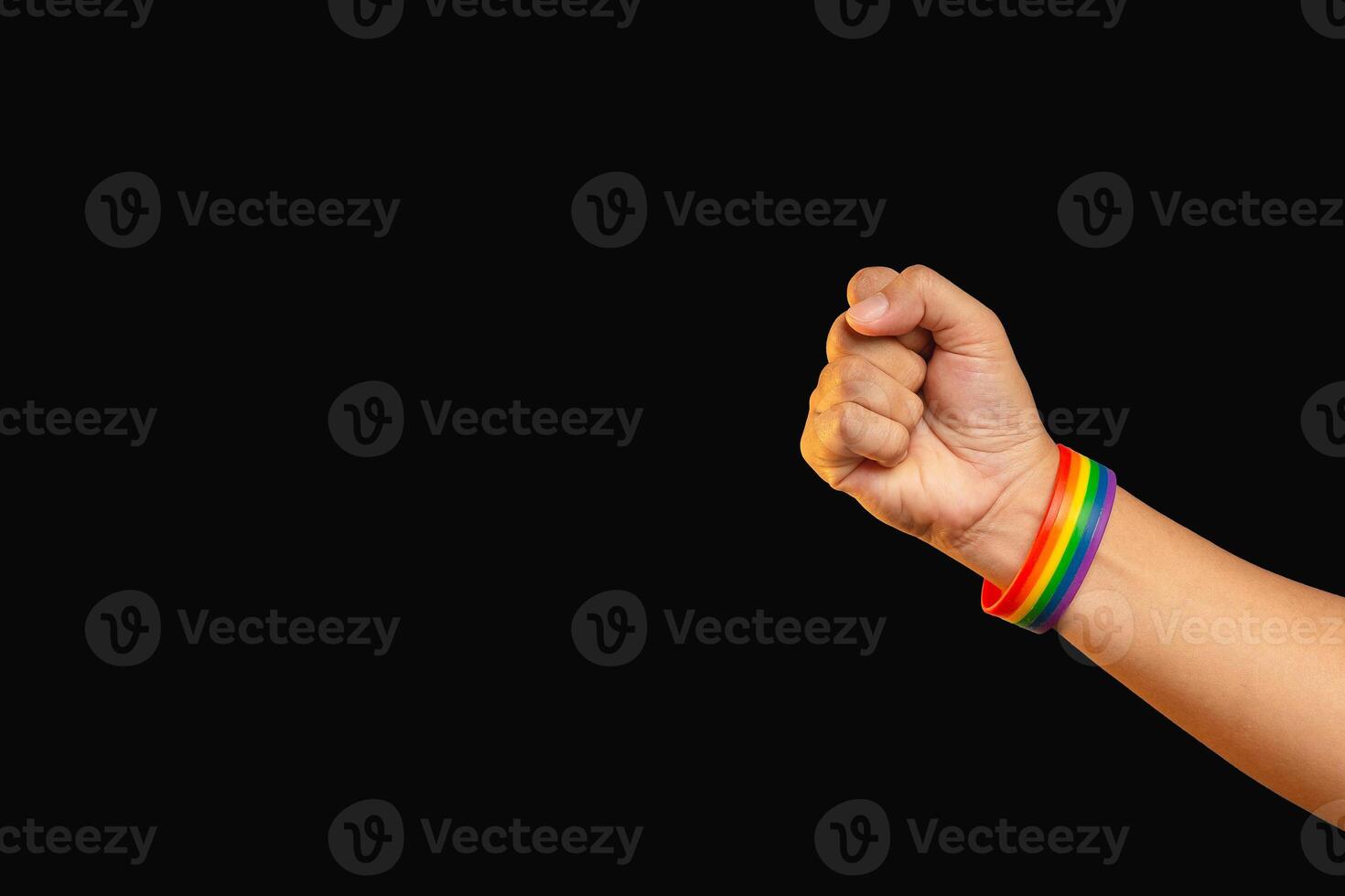 Close-up of a hand fist with rainbow wristband in a hand while standing against a black background. photo
