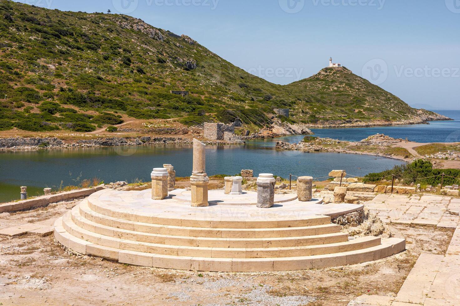 The Ancient ruins on hillside overlooking the sea in Turkiye. Stone structures and columns are visible, surrounded by greenery and rocky terrain photo