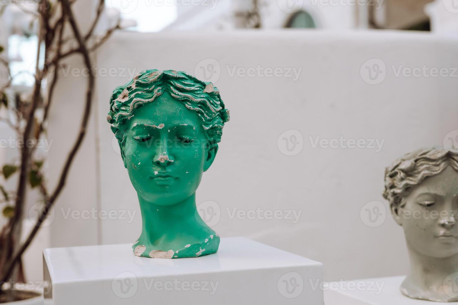 Unique sculptural display of green and white busts on white pedestals in an outdoor setting. photo