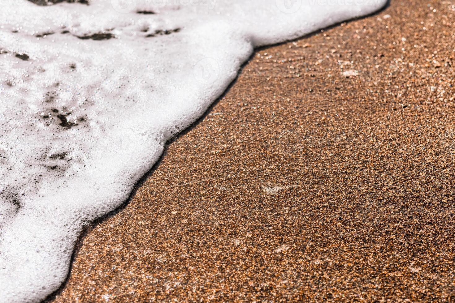 Close-up of sandy beach with gentle waves lapping at the shore. sand is light brown and textured, with white foam from the water. photo