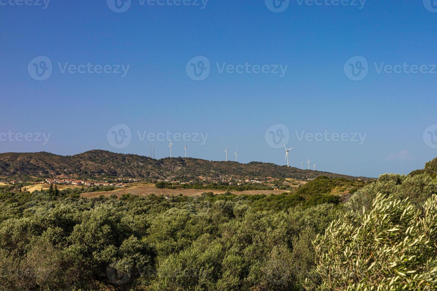 A scenic view of rolling hills in Turkiye, featuring green vegetation and wind turbines against a clear blue sky. photo