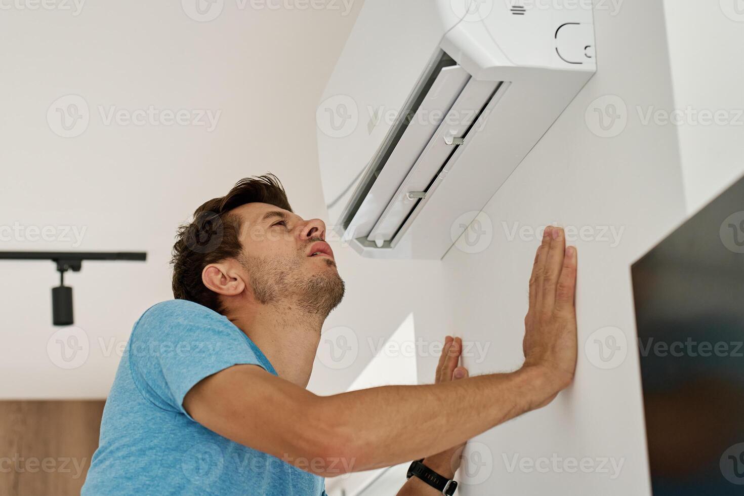 Man enjoying cool air from air conditioner at home photo
