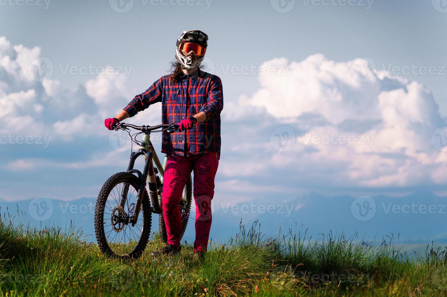 Unrecognizable athlete in protective gear standing in a field and looking at the camera against the backdrop of foggy mountains and cumulus clouds. Mountain sports concept photo