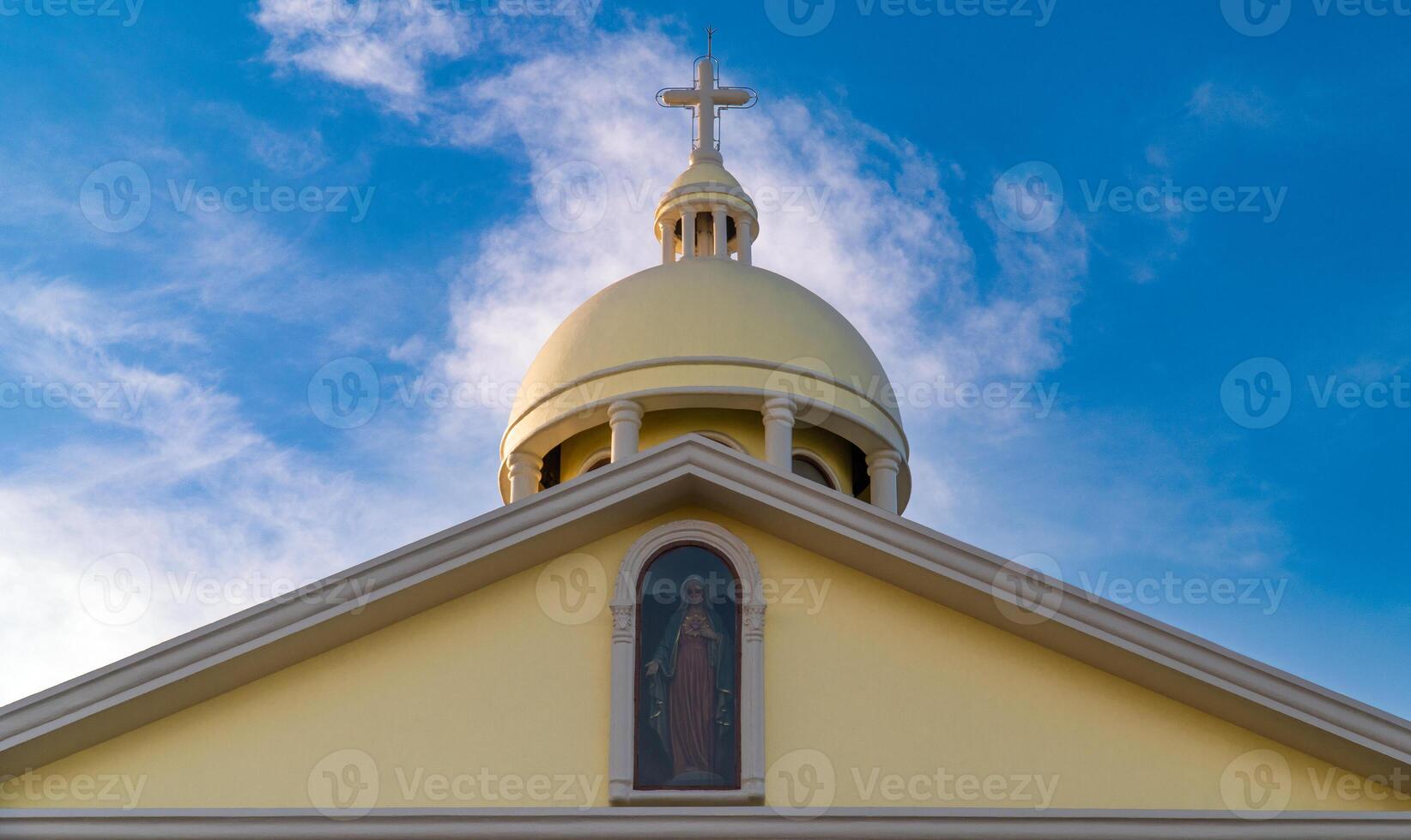 White and yellow church in Christianity has dome and cross on the top. With a statue of the Lord Mary in front of the gable. photo