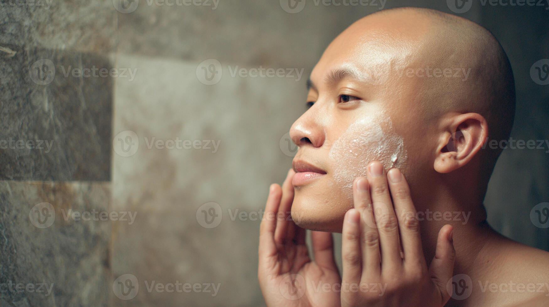 Non binary person applying skincare product while standing in modern bathroom with stone walls during evening routine photo