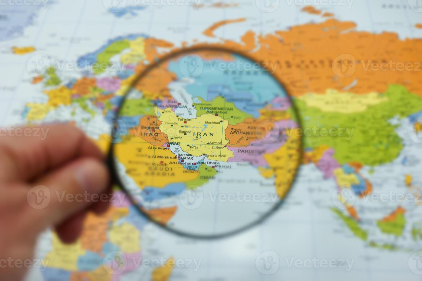 Hand holding magnifying glass over a world map highlighting Iran's location and geography details photo