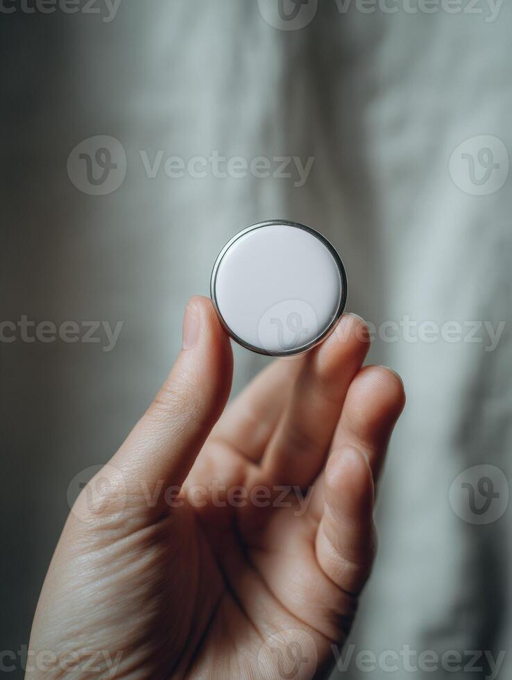Close-up of hand holding a small round button or coin against a neutral background photo