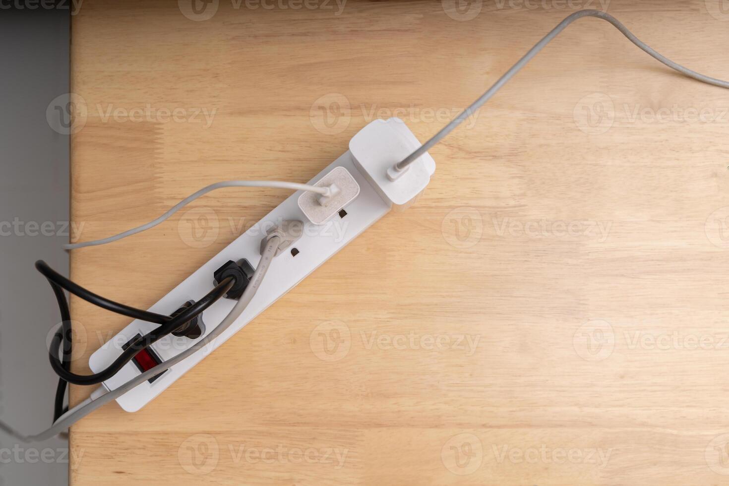 Top view of power strip with multiple plugs and tangled cables on wooden desk, electricity and energy concept photo