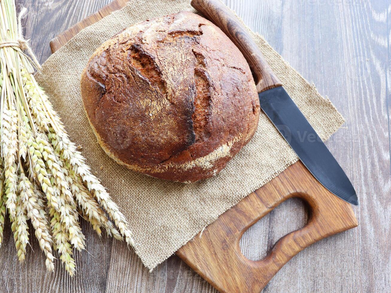Rustic crusty bread loaf with some wheat ears on dark wood background . photo